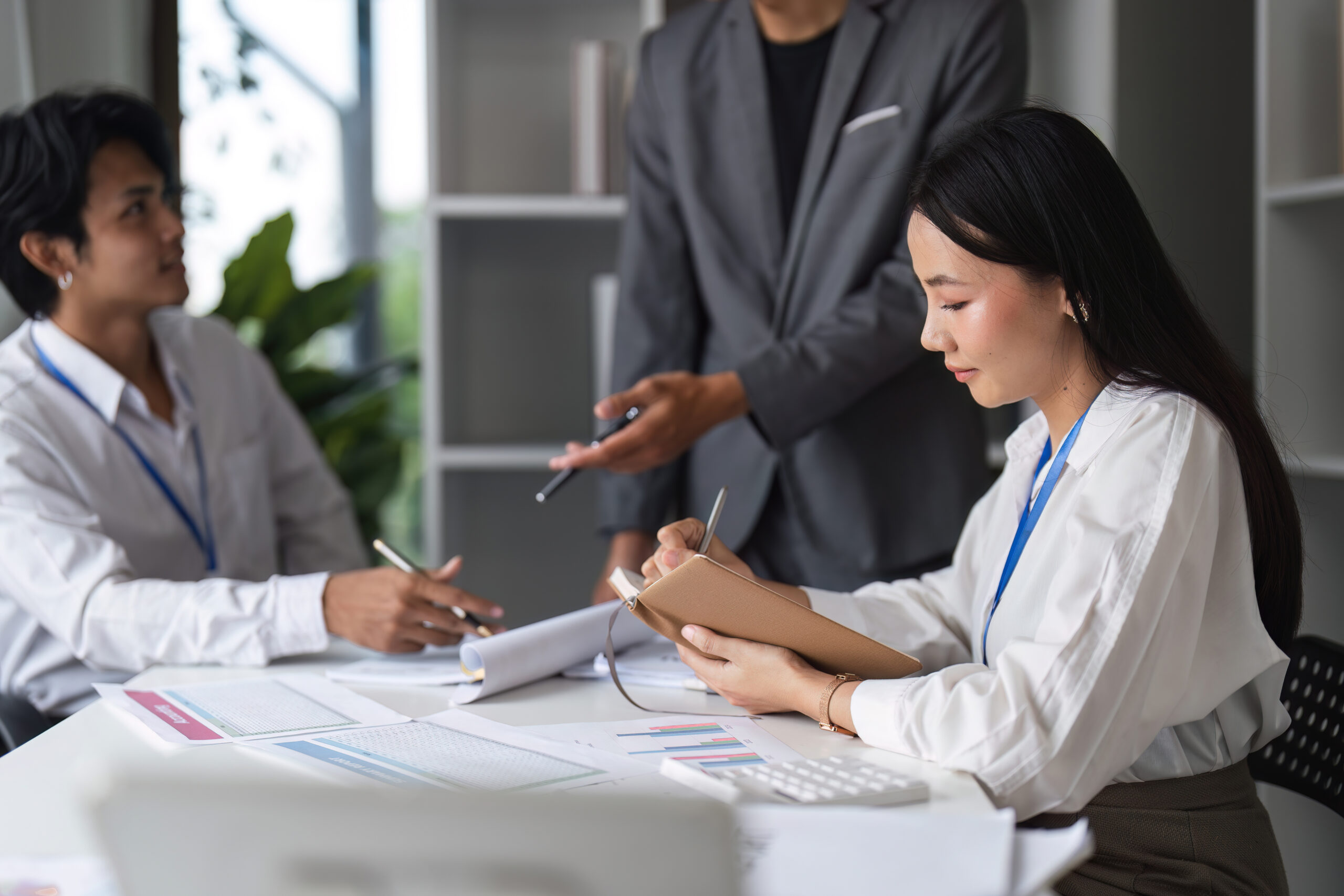 Professional business people collaborating in a modern office setting, engaged in a meeting and taking notes.
